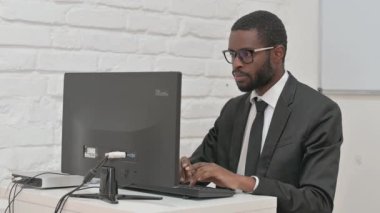 Bilgisayar üzerinde çalışırken kameraya bakan kendinden emin iş adamı