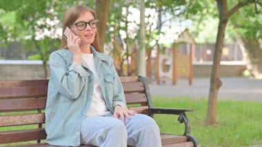 Park ortamında akıllı telefondan konuşan genç bir kadın.