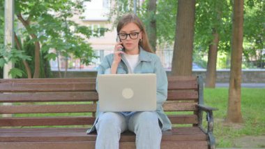 Dışarıda otururken bilgisayarla konuşan kadın.