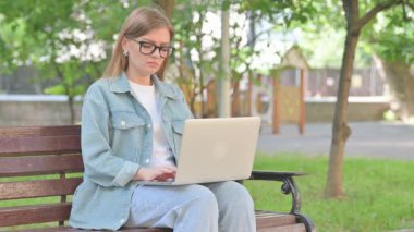 Park yerinde dizüstü bilgisayar kullanırken boynu ağrıyan genç bir kadın.