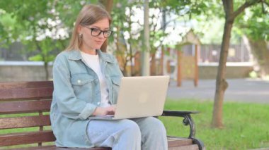Dizüstü bilgisayarlı neşeli genç kadın Park Bench 'te kazanmanın tadını çıkarıyor.