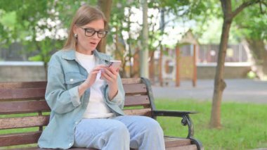 Park bankında telefon kullanırken Genç Kadın Heyecanını İfade Ediyor