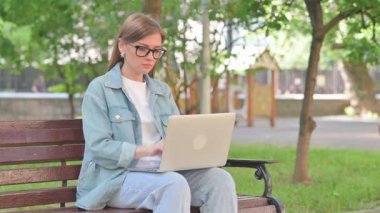 Dizüstü bilgisayarla Bench 'ten çıkan genç kadın.