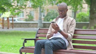 Park bankında telefon kullanan genç Afrikalı adam.