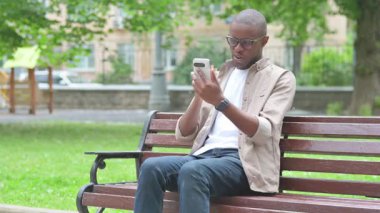 Genç Afrikalı Adam Park Bench 'te telefon görüşmesi yapıyor ya da konferans veriyor.
