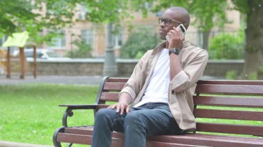 Park ortamında akıllı telefondan konuşan genç bir Afrikalı.