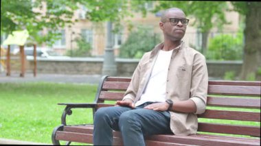 Bekleyen Afrikalı genç adam Park Bench 'i kontrol ediyor.