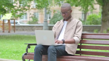 Park Bench 'te dizüstü bilgisayar kullanan genç Afrikalı adam.