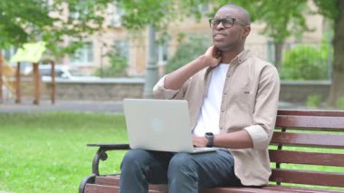 Park 'ta dizüstü bilgisayar kullanırken boynu ağrıyan genç bir Afrikalı.