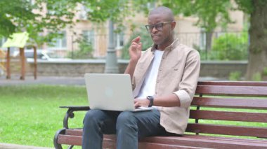 Park Bench 'te dizüstü bilgisayarı olan stresli bir Afrikalı.
