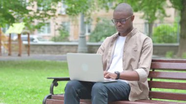 Park 'ta dizüstü bilgisayar kullanırken öksüren hasta Afrikalı genç adam.