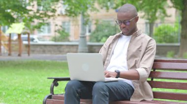 Park Bench 'te dizüstü bilgisayar kullanan kafası karışmış bir Afrikalı.