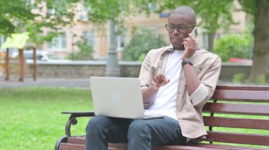 Young African Man Talking on Phone While Using Laptop