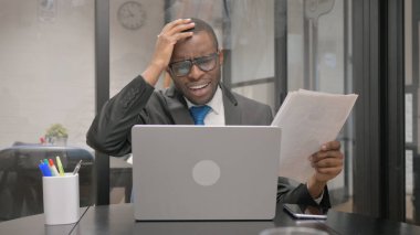 Belgeler ve Dizüstü bilgisayar üzerinde çalışan şoke olmuş Afrikalı İşadamı