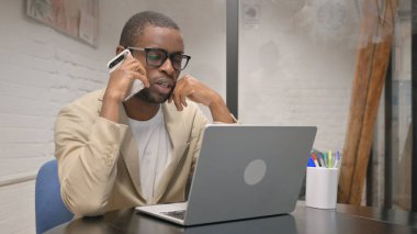 Bilgisayarda çalışırken telefonda konuşan Afrikalı Adam