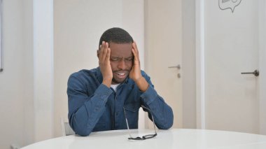 Baş ağrısı olan genç bir Afrikalı iş yerinde oturuyor.