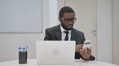 dizüstü bilgisayarda çalışırken akıllı telefon kullanan işadamı