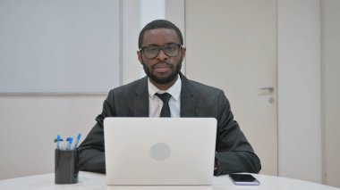 Afrika kökenli Amerikalı iş adamı ofisteyken kameraya bakıyor.