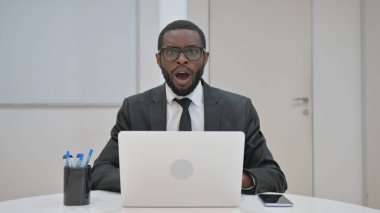 Ürkmüş Afrikalı Amerikalı iş adamı kameraya bakarken şaşkın şaşkın bakıyor.