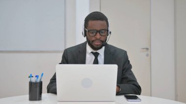 Kulaklık takan ve dizüstü bilgisayarda çalışan bir iş adamı.