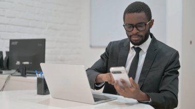 dizüstü bilgisayarda çalışırken akıllı telefon kullanan işadamı