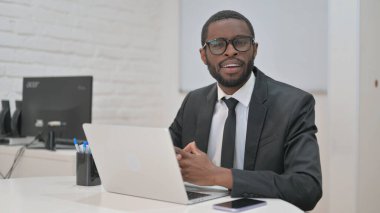 Gülümseyen Afrikalı Amerikalı işadamı ofisteyken kameraya özgüvenle bakıyor.