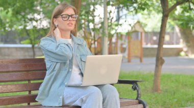 Park yerinde dizüstü bilgisayar kullanırken boynu ağrıyan genç bir kadın.