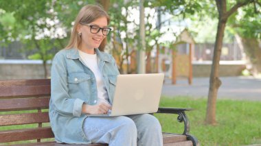 Park 'taki laptopta video görüşmesi yapan genç bir kadın.