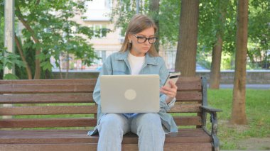Açık havada otururken Akıllı Telefon ve Laptop Kullanan Kadın