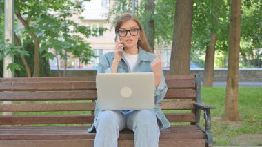 Dışarıda otururken bilgisayarla konuşan kadın.