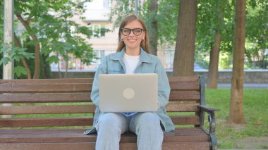 Dışarıda otururken dizüstü bilgisayarla gülümseyen sıradan bir kadın.