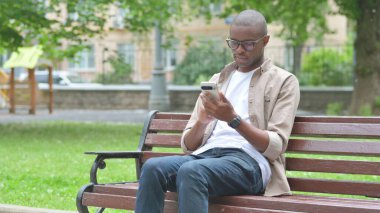 Park bankında telefon kullanan genç Afrikalı adam.
