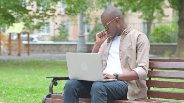 Park 'ta dizüstü bilgisayar kullanırken öksüren hasta Afrikalı genç adam.