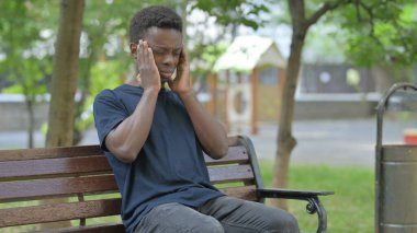 Açık havada oturan baş ağrısı olan Afrikalı Amerikalı adam.