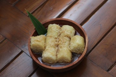 a close up of lupis with grated coconut and brown sugar sauce served in a wooden bowl. Indonesian traditional food photo concept.