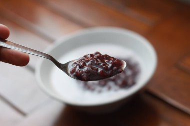 a close up of a bowl of black sticky rice porridge with coconut milk ready to eat. Indonesian traditional food concept.