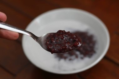 a close up of a bowl of black sticky rice porridge with coconut milk ready to eat. Indonesian traditional food concept.