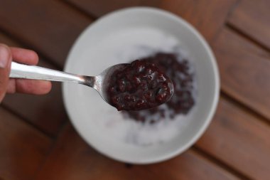 a close up of a bowl of black sticky rice porridge with coconut milk ready to eat. Indonesian traditional food concept.