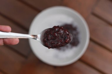 a close up of a bowl of black sticky rice porridge with coconut milk ready to eat. Indonesian traditional food concept.