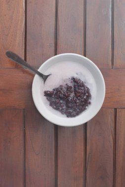 a close up of a bowl of black sticky rice porridge with coconut milk ready to eat. Indonesian traditional food concept.