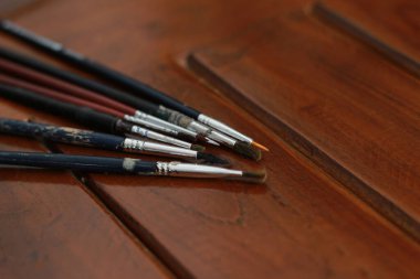 a close up of several painting brushes isolated on a natural patterned wooden background. concept photo art.