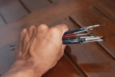 a close up of several hand-held painting brushes isolated on a natural patterned wooden background. concept photo art.