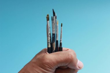 a close up of a hand holding a painting brush isolated on a blue background. concept photo art.