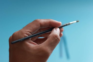 a close up of a hand holding a painting brush isolated on a blue background. concept photo art.
