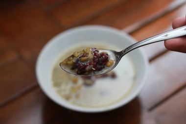 a close up of a bowl of green bean porridge and black sticky rice doused in coconut milk, served warm and ready to eat on a wooden background with a natural pattern. Indonesian food concept.