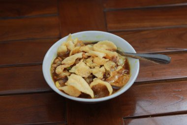 a close up of a ready-to-serve bowl of chicken porridge with a natural patterned wooden background. Indonesian food concept.