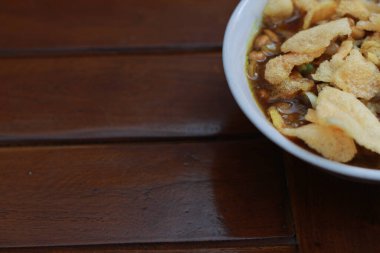 a close up of a ready-to-serve bowl of chicken porridge with a natural patterned wooden background. Indonesian food concept.