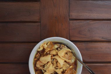 a close up of a ready-to-serve bowl of chicken porridge with a natural patterned wooden background. Indonesian food concept.