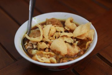 a close up of a ready-to-serve bowl of chicken porridge with a natural patterned wooden background. Indonesian food concept.