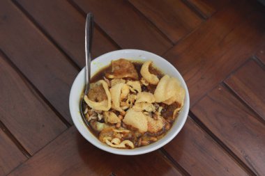 a close up of a ready-to-serve bowl of chicken porridge with a natural patterned wooden background. Indonesian food concept.